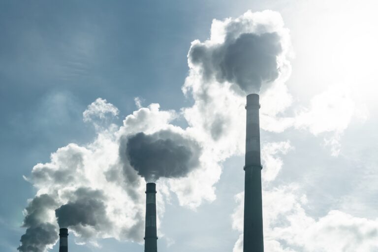 Three smoke stacks blow smoke into the sunny sky